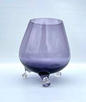 Purple-tinted Swedish art glass bowl with three clear tripod feet, viewed at an angle to show shape and foot details.