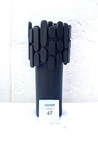 Front view of black brutalist ceramic vase showing textured upper rim and smooth cylindrical body with white label in front.