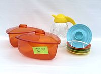 View of entire lot with two orange Tupperware triangular bowls with lids, a clear juice pitcher with yellow handle, and four colorful egg holders stacked on a rack.