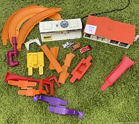 Overview of Hot Wheels Sizzlers Power Pit buildings, orange track and launcher pieces, and three diecast cars arranged on green carpet.