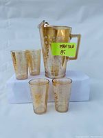 Full set showing pitcher and four glasses in carnival glass with etched floral pattern.