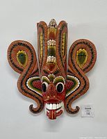 Front facing view of the hand carved and painted wooden mask showing full detail of the face and curling side elements