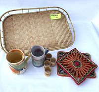 Contents laid out including rattan tray, pottery mugs, bamboo napkin rings, and embroidered trivets.
