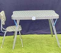 Full side view of vintage Arbrite table and chair set on grass with black backdrop showing patterned laminate surfaces and chrome legs.