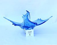 Bright blue stretch art glass sculpture with a flowing, organic form and elongated wing-like extensions shown from a frontal perspective.