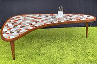 Full view of kidney-shaped coffee table with decorative mosaic tile top and three tapered wood legs on green carpet