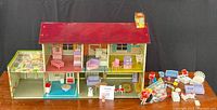 Front view of the three-level vintage MARX tin litho dollhouse with various colorful interiors and exterior details, showing furniture pieces inside and dolls seated outside on the right.