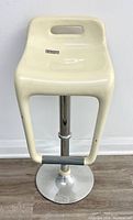 Full front view of white molded plastic bar stool with chrome pedestal base and footrest bar, showing overall shape and condition.