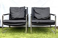 Front view of two identical armchairs showing black leatherette cushions with visible wear, set on green carpeted floor against white backdrop.