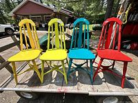Four colorful wooden kitchen chairs on a flat cart outdoors, colors yellow, lime green, teal, and red visible.