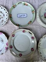 Close-up of two plates: one with green rim and orange flowers, another with cutout handles and pink rose floral design.
