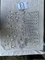 Top-down photo showing an assortment of clear glass prisms laid out on a white towel, including teardrop shapes and some rounder multifaceted shapes with metal loops.