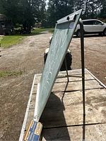 Folding chalkboard standing on a wooden surface outdoors, viewed from side angle showing metal frame and chalkboard surface.