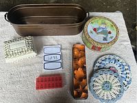 Copper planter, cookie tins, metal cookie cutters, crocheted hot pads, small ceramic planter displayed on beige fabric