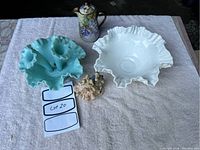 Wide view of two Fenton hobnail glass pieces, hand-painted pot, and figurine on white towel