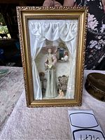 Front view of the glass-front shadowbox containing the lady figurine in vintage attire with satin curtains and miniature interior furniture.