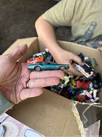 Close-up of teal colored muscle car held in hand with many toy cars visible in the background inside the box.