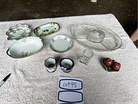 Full set of Nippon dishes including three floral porcelain dishes, glass pickle dish with lid, two small blue-rimmed floral porcelain cups, clear glass jar, glass boot-shaped cup, and ceramic salt and pepper shakers shaped like peaches on a green base.