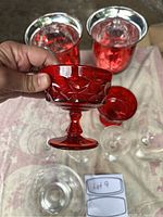 Close-up of one red footed glass with patterned design held in hand, other red glasses in background