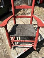 Close-up view of the chair seat showing the woven seating area and red wooden frame with some weathering and paint wear.