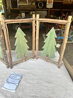 Front view of the rustic wooden folding Christmas decor with two green tree cutouts in natural bark frames.