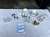 Full overview of salt and pepper shakers, tea cups, sugar bowl, and figurine on a cloth surface