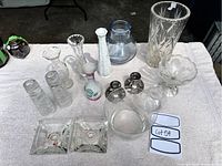 Photo of various glass and ceramic vases, candle holders on display on a white fabric surface