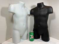 Photo showing two child mannequin torsos, one white and one black, with a 7up can for scale to illustrate size. Both have hollow backs and no heads.
