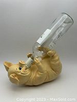 Pig resin sculpture holding a wine bottle by its mouth while lying on its back.