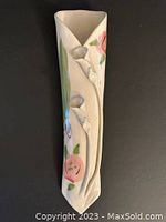 Front view of ceramic wall pocket showing pink painted flowers and 3D lily flower reliefs on cream-colored ceramic surface.