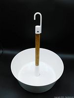 White circular steel flower pot with a central bamboo pole topped with a white hook for hanging, shown from the front against black background.