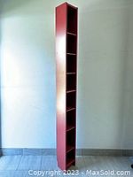 Tall and slim red storage cabinet viewed from an angled side showing overall height and slim profile, six shelving spaces visible.
