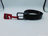 Black rolled leather belt with black metal buckle and red Levi's brand tags attached, displayed against white background