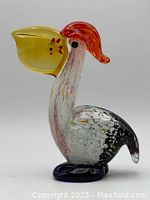 Color view of the glass pelican showing its yellow beak with fish, red crest, and mottled white and black body on blue glass base