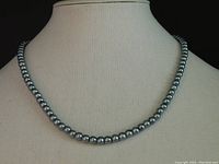 Front view of the dark gray and black pearl necklace displayed on a beige mannequin, showing the pearl strand with uniform dark and light reflective pearls.