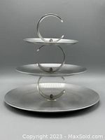 Side view of the three-tiered brushed aluminum serving tray with visible wear and ribbed curved handles connecting each tier.