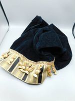 View of black towel showing gold and black striped fabric skirt with gold cording and tassels along edge