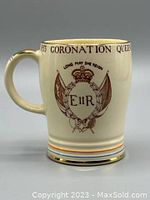 Front side of the cream-colored mug with Queen's emblem 'Long May She Reign' and gold trim