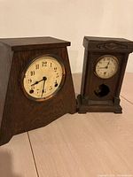 Front view of both clocks showing shapes, dials, and wood finishes side by side