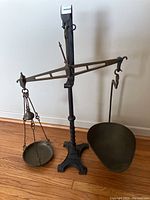 Full view of antique Victorian balance beam scale showing wrought iron base and upright column, brass beam with hanging pans.
