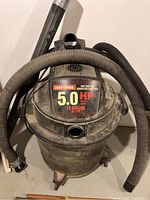 Front view of Craftsman wet/dry vacuum showing attached hose, dust on unit, and wheel base.