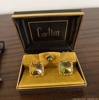 Set of two gold coloured square cuff links and one matching stud with colored centre stones, housed in a yellow velvet lined Carlton case.