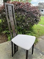 Single modern dining chair shown outdoors with dark metal backrest featuring square cutouts and white upholstered seat.