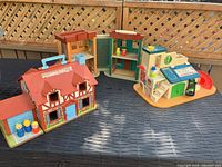 Three Fisher Price Sesame Street plastic playsets on table. Included are a family home, clubhouse with slide, and a tall building.