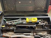Open metal toolbox showing assortment of wrenches, pliers, and yellow Stanley measuring tape