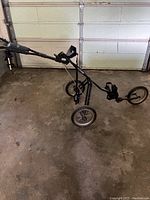 Full side view of the black Golf Bag Boy push cart with three wheels, showing frame and tires.