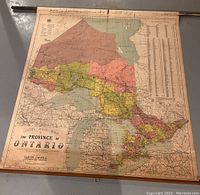 Full view of large wall map of Ontario spread out on floor showing colored regions and wooden mounting rods.