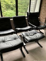 Overall view of four black leather sling-back chairs and two matching ottomans on a balcony.