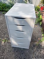 Front view of white 5-drawer organizer on outdoor pavement, showing smooth finish and drawer handles.