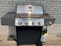 Full view of the stainless steel propane BBQ with four main burner knobs, side burner, propane tank attached, and wheels for transport.